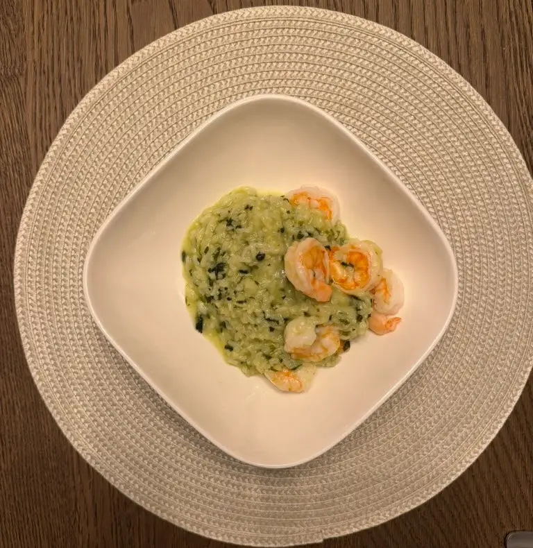 Risotto de espinaca con camarones en plato blanco sobre mantel en mesa de madera oscura.